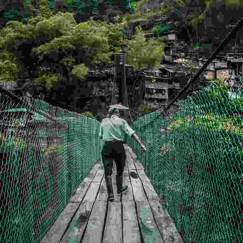 Man walking over hanging bridge with wooden planks in poverty-stricken Colombian town.