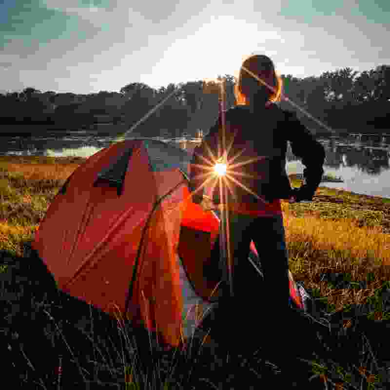 Camper rises out of tent early in the morning in the woods.