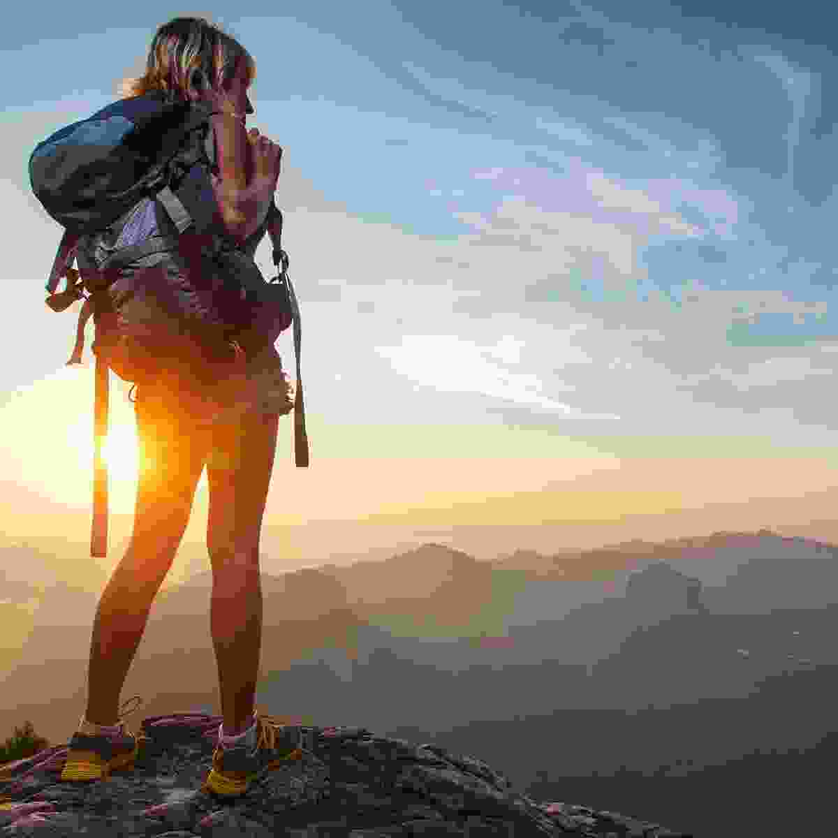 A woman stands on top of a large ridge looking out over a huge valley.