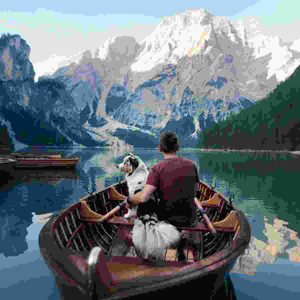 A man and his dog in a canoe on peaceful waters and a large mountain in the background.