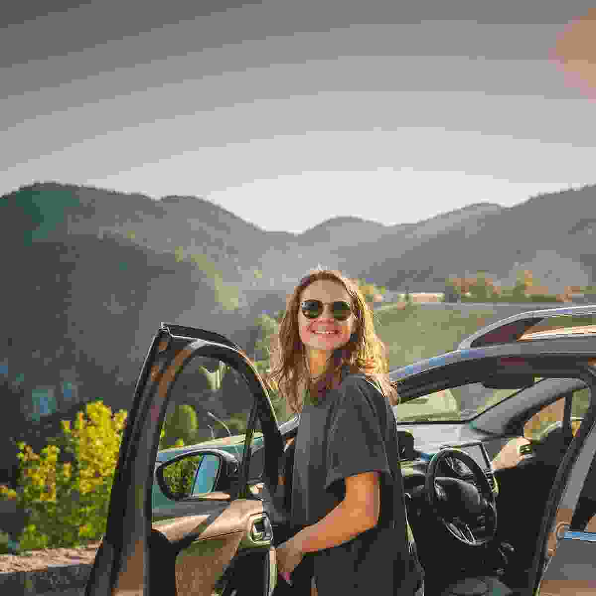 Woman opens her car door to view the mountain scenery.