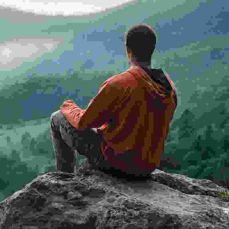 A man sitting on a ridge overlooking a great valley.