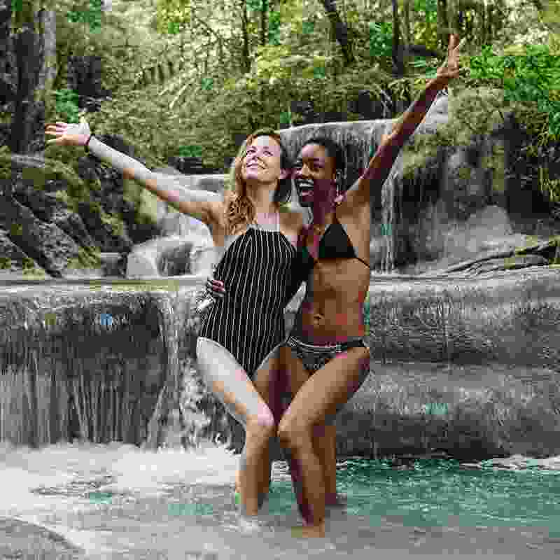 Interracial friends enjoy a photo shoot at a small waterfall in a Colombian jungle.