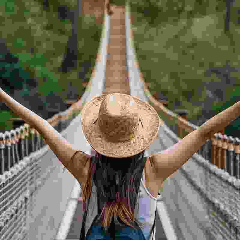 Excited American woman crosses a high hanging bridge in the jungle of Colombia.