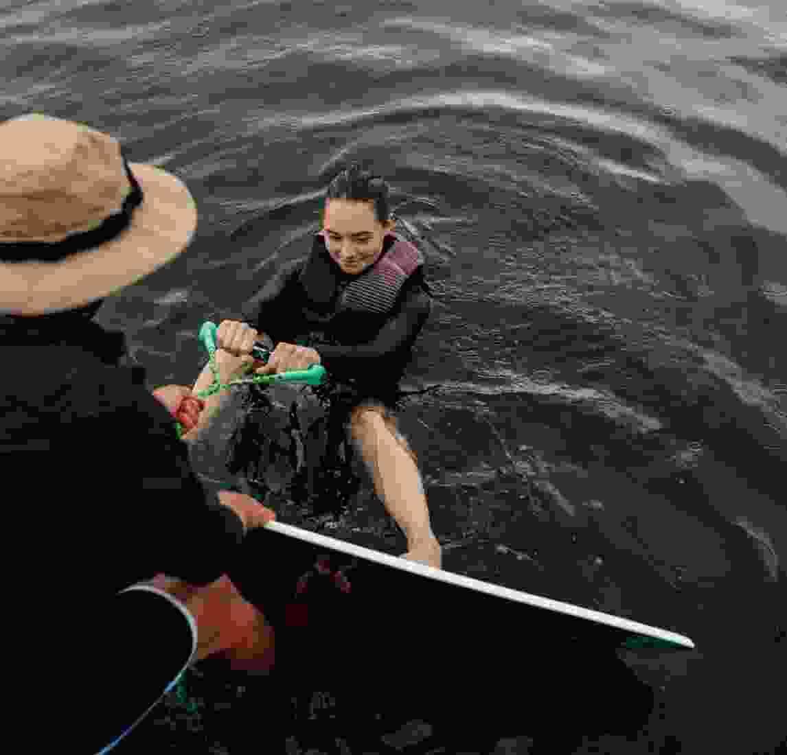 A lady listens to instructions from her kiteboarding guide as she sits in the water waiting for her boat to leave.