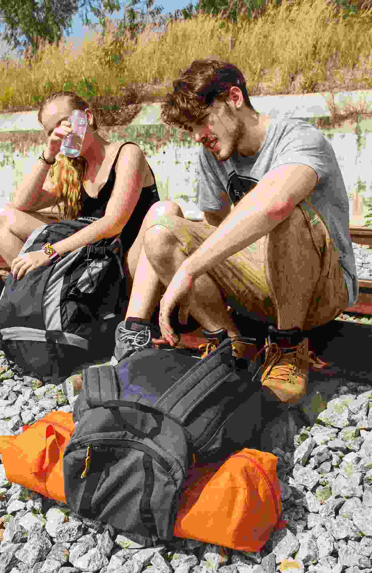 A hiking couple sit on the railroad tracks on a hot day for a little rest and hydration.