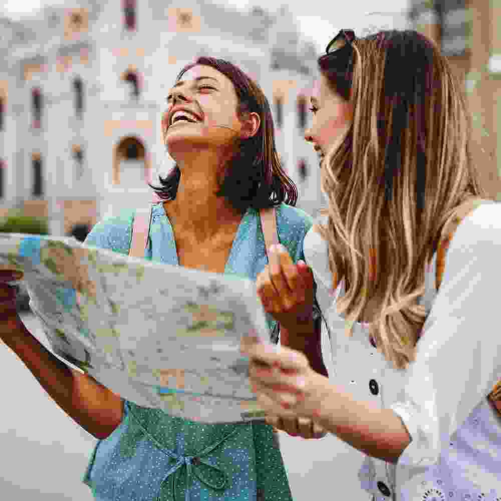 Two vacationing Western women consulting a paper map on vacation.