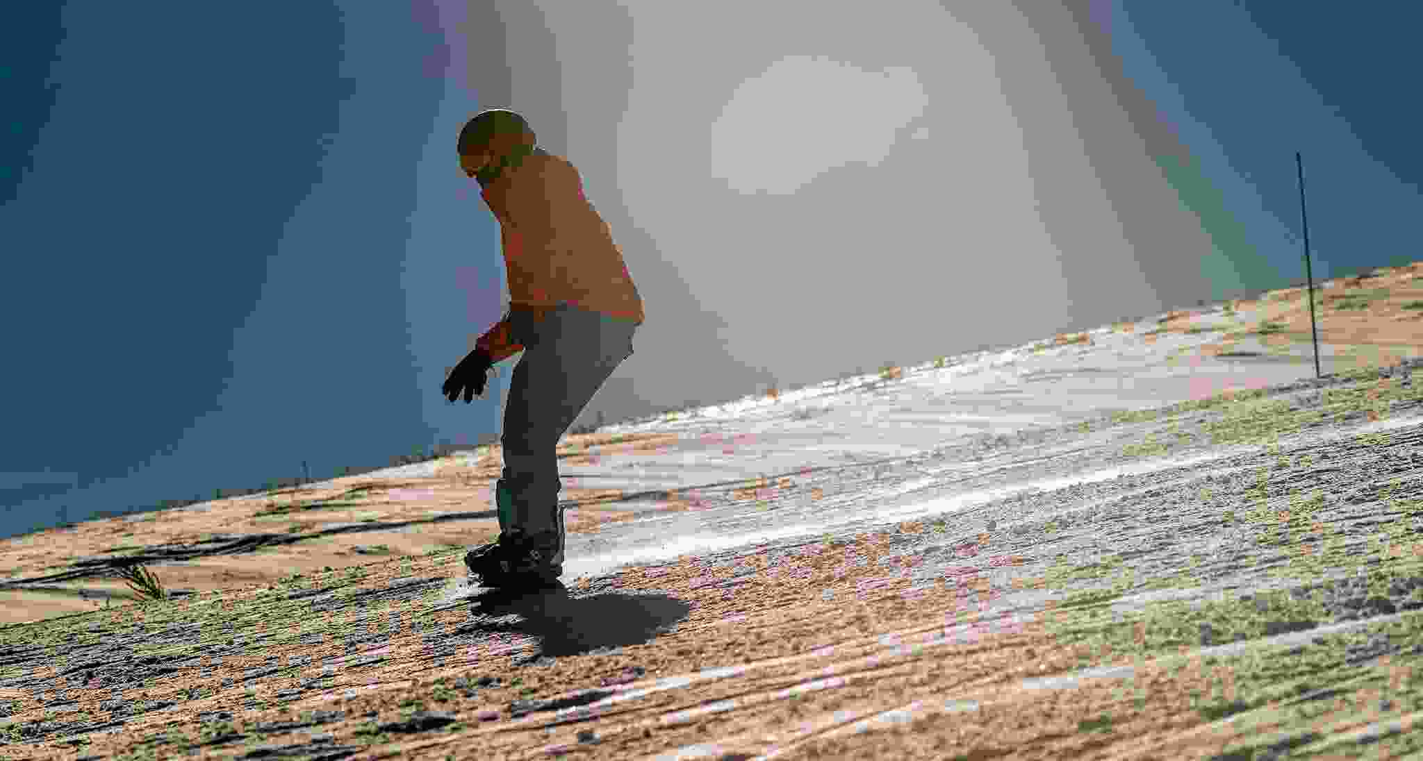 Optically illusive man snowboarding on grassy hill.