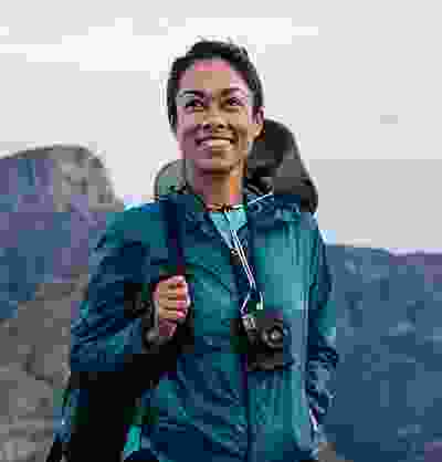 Pleasantly elated native woman with backpack and camera enjoying a nature hike.