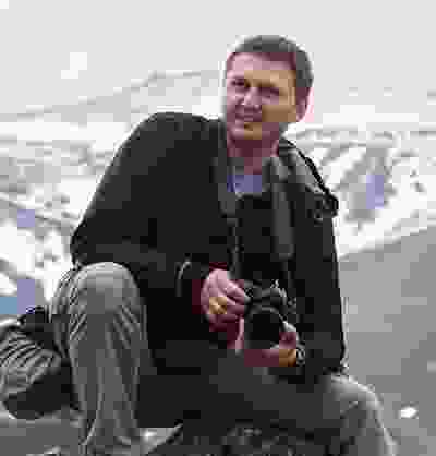 A Western man photographing the world from the top of a very high mountain.