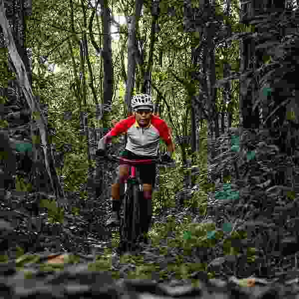 Asian bicycle enthusiast riding a bicycle off-trail in equatorial jungle.